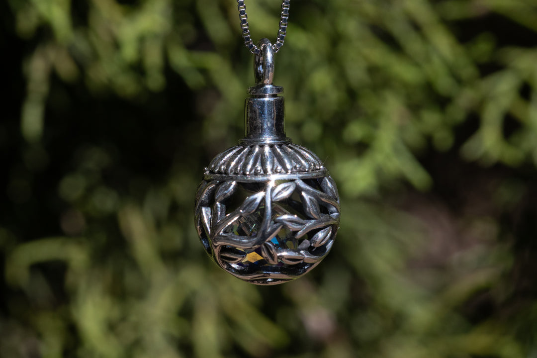 Silver ball cremation pendant with a leafy lattice design and a colorful crystal inside on a silver chain
