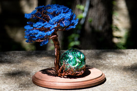 glass cremation orb with wire tree of life sitting on wood base outside un