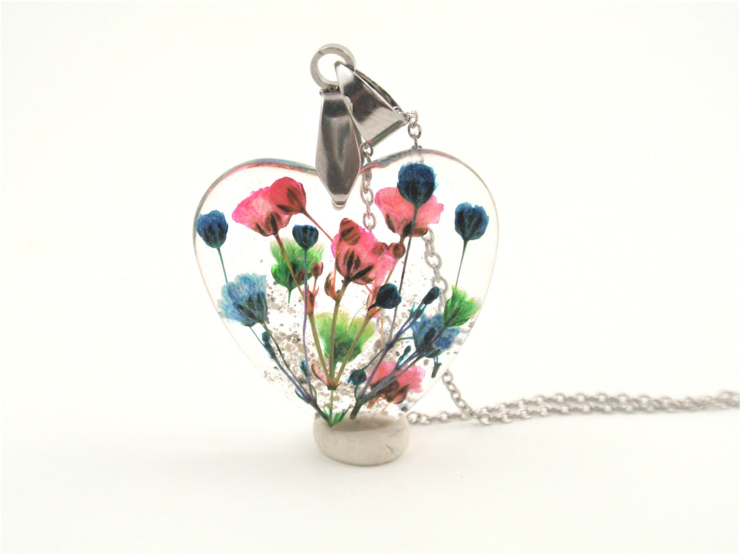Heart shaped clear resin pendant with pink blue and green dried flowers on a silver chain