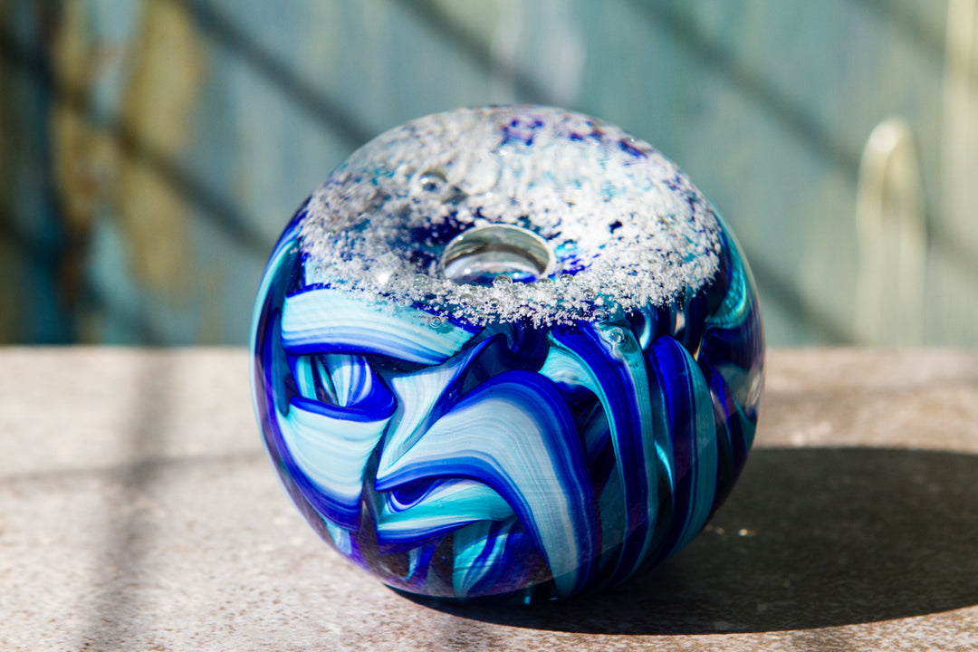 Donut shaped blue glass memorial paperweight infused with cremains featuring white frost on top and bright ribbon swirls