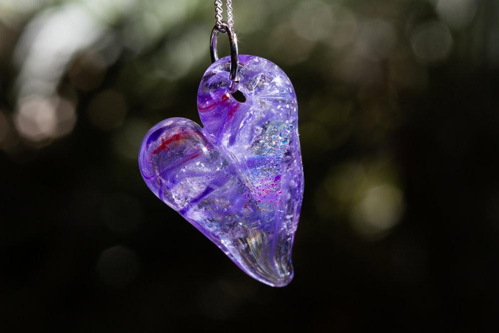 Purple glass heart cremation pendant suspended on a chain with ashes encased inside