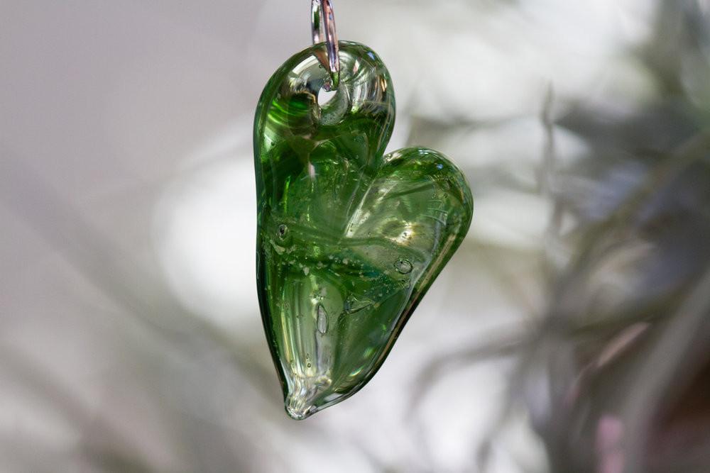 Green glass heart cremation pendant with ash infusion shown in a close up against a soft background