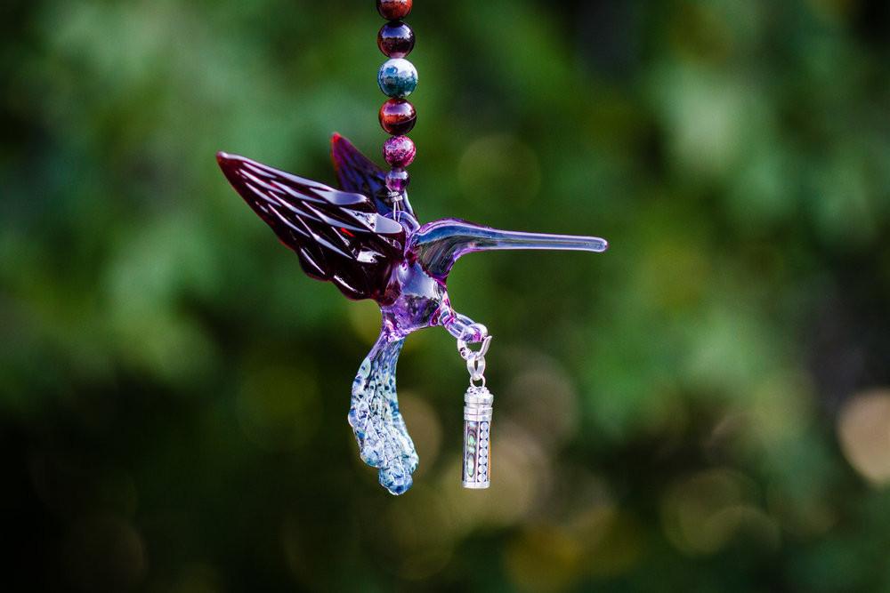 Purple glass hummingbird with crystal butterfly accent and dangling keepsake urn alongside a blue marbled stone charm
