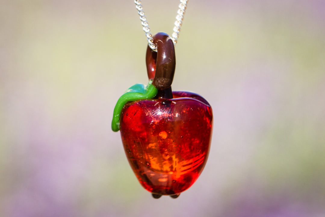 Red glass apple pendant infused with cremation ashes, with a brown stem and green leaf on a silver chain.