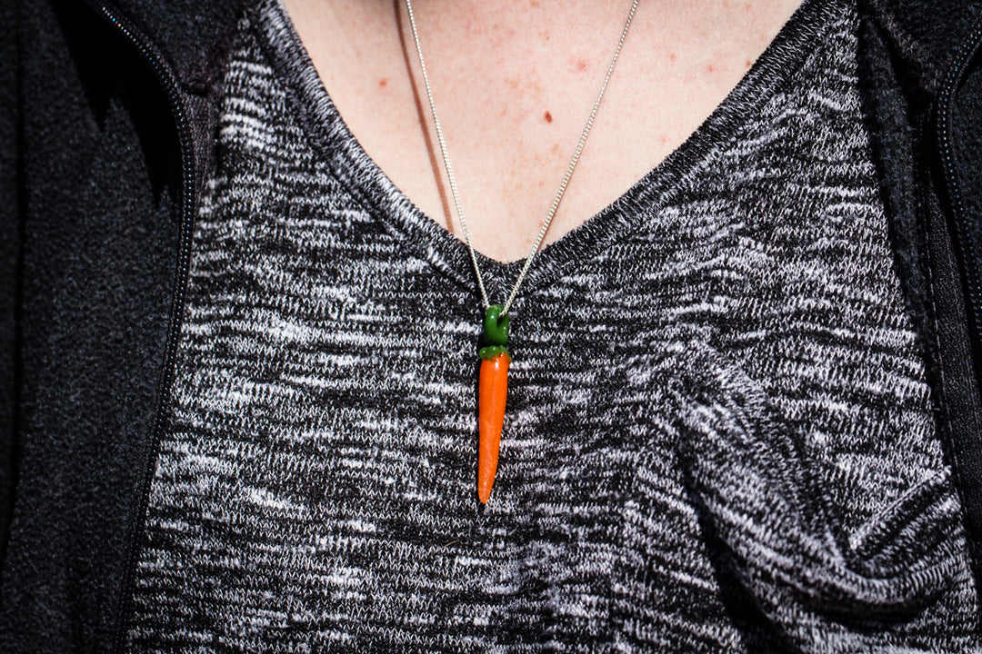 Orange glass carrot pendant with cremation ash and green top on a silver chain worn around the neck against a gray patterned sweater