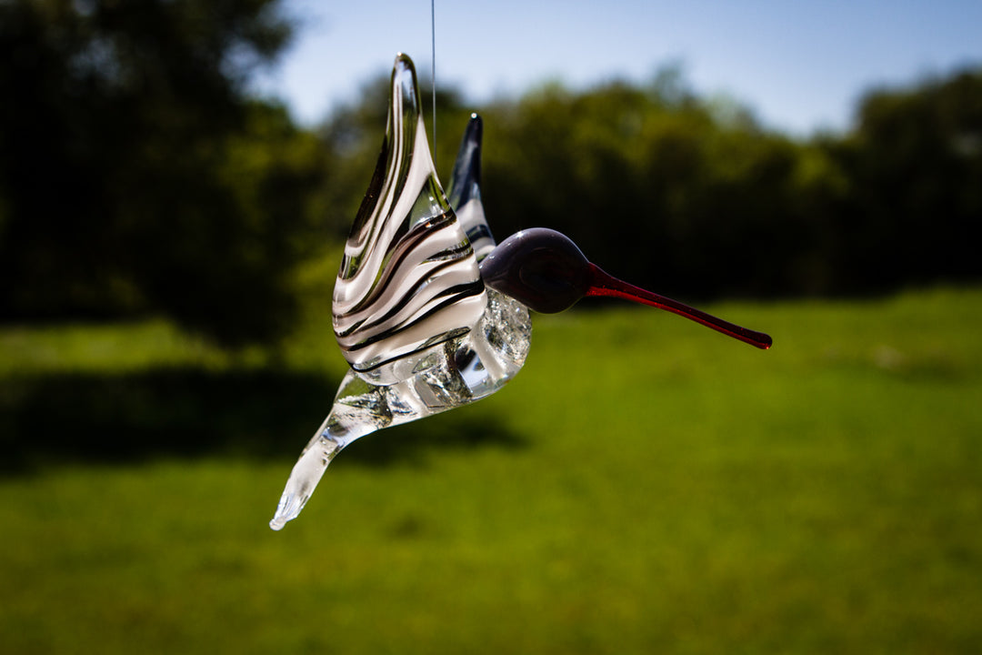 Glass hummingbird with black and white swirls and a red beak, hanging in daylight.