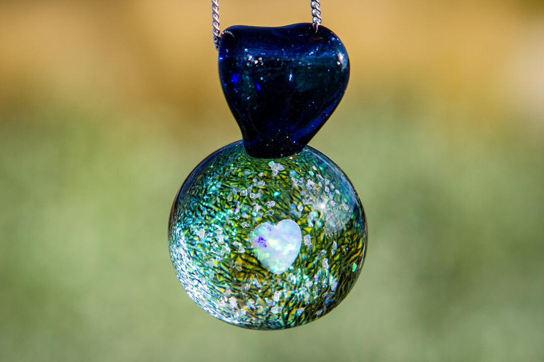 Blue heart shaped pendant atop a green speckled glass orb containing a white heart opal