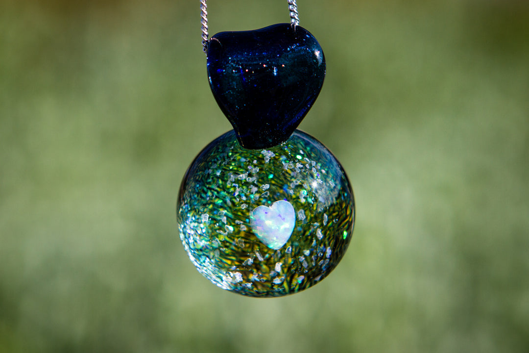 Blue heart shaped top over a green speckled glass orb with a white heart opal, pendant on a silver chain