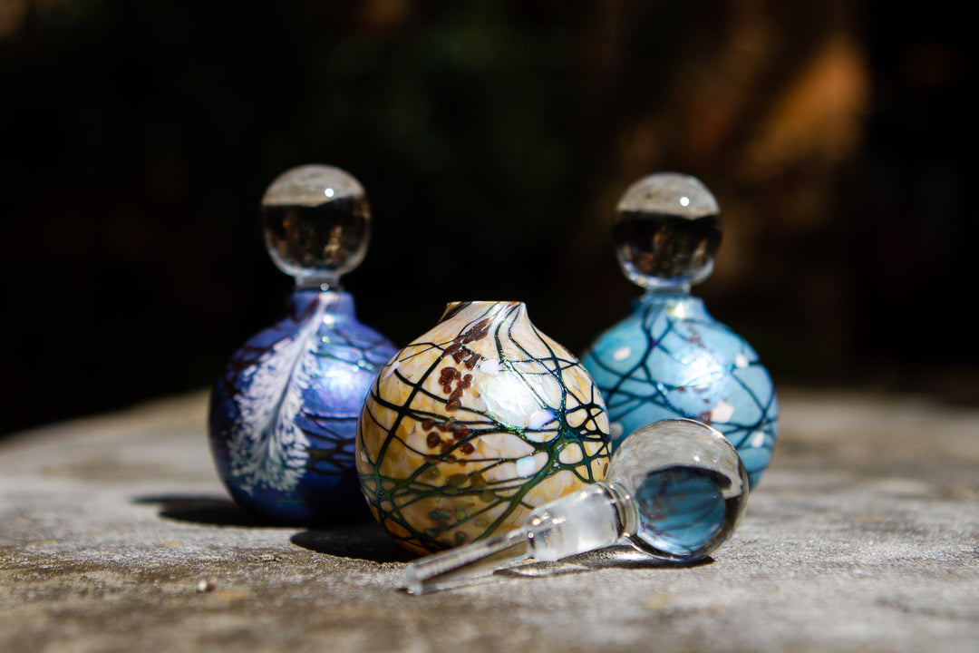 Fancy glass keepsake urns for cremation ashes foreground yellow urn with a black lattice pattern and blue urns in the background