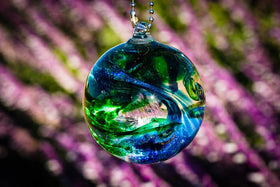 blue and green glimmer orb hanging in sun in front of purple flowers