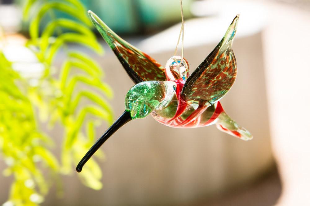 Green and red glass hummingbird ornament infused with cremation ashes and a hanging hook on top.
