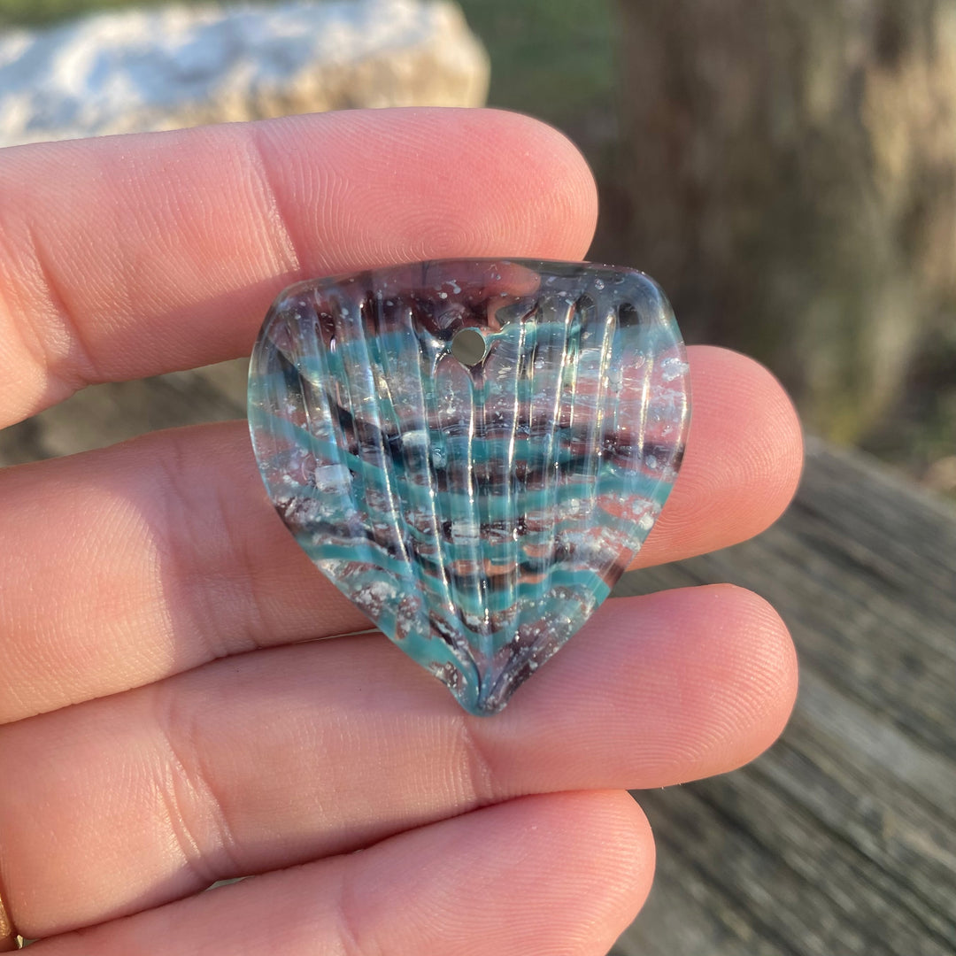 Ash infused borosilicate glass guitar pick with blue green swirls held between fingers