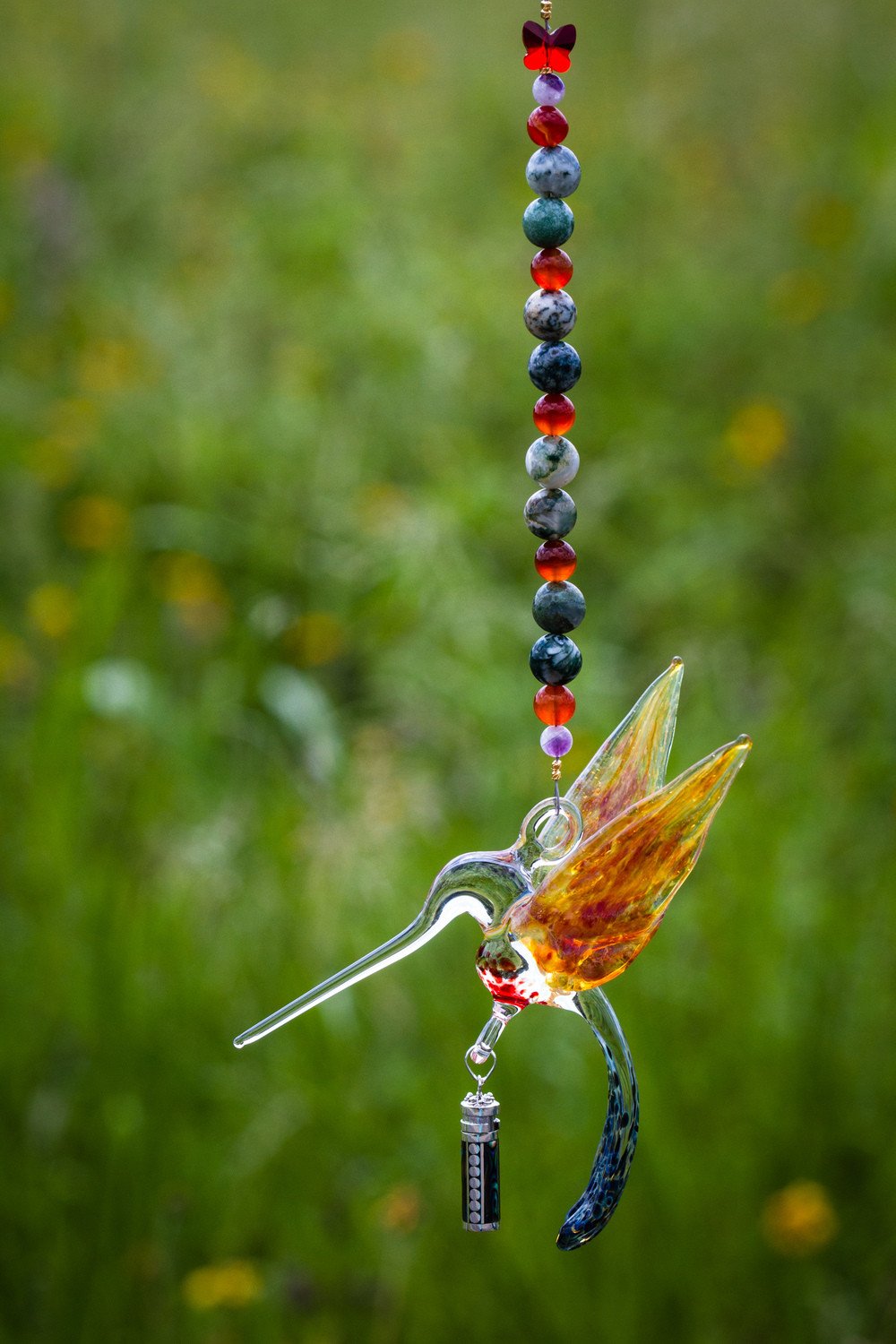 Yellow orange glass hummingbird pendant with a long beak blue speckled tail and a hanging beaded strand with a keepsake vial