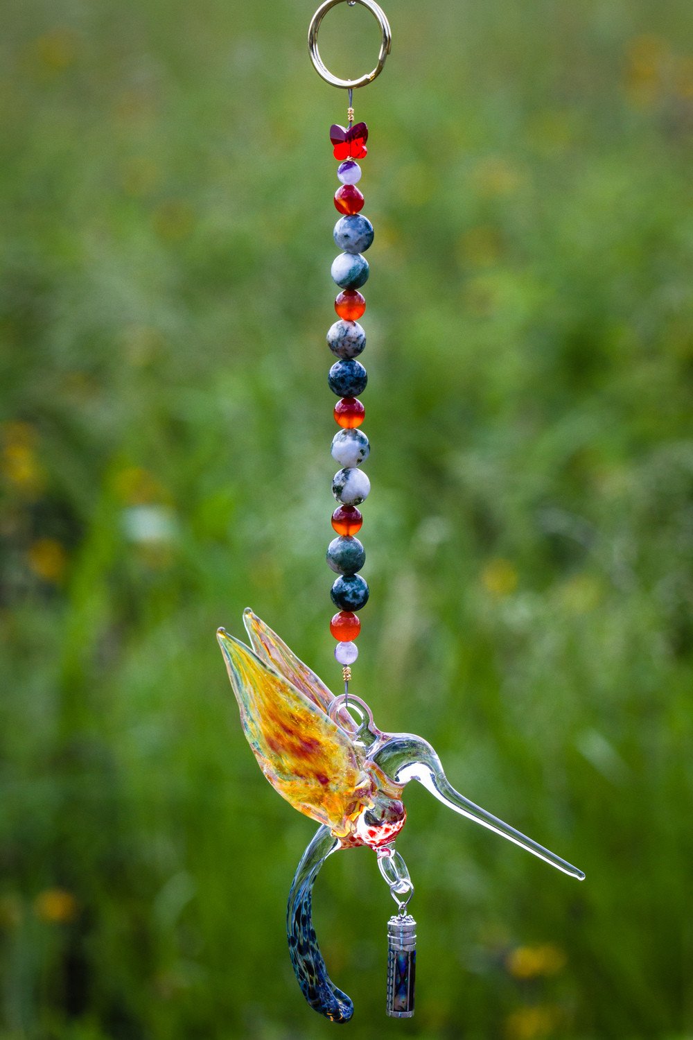 Beaded charm with ring at top and a hanging glass hummingbird pendant along a string of multicolored beads and a vial charm