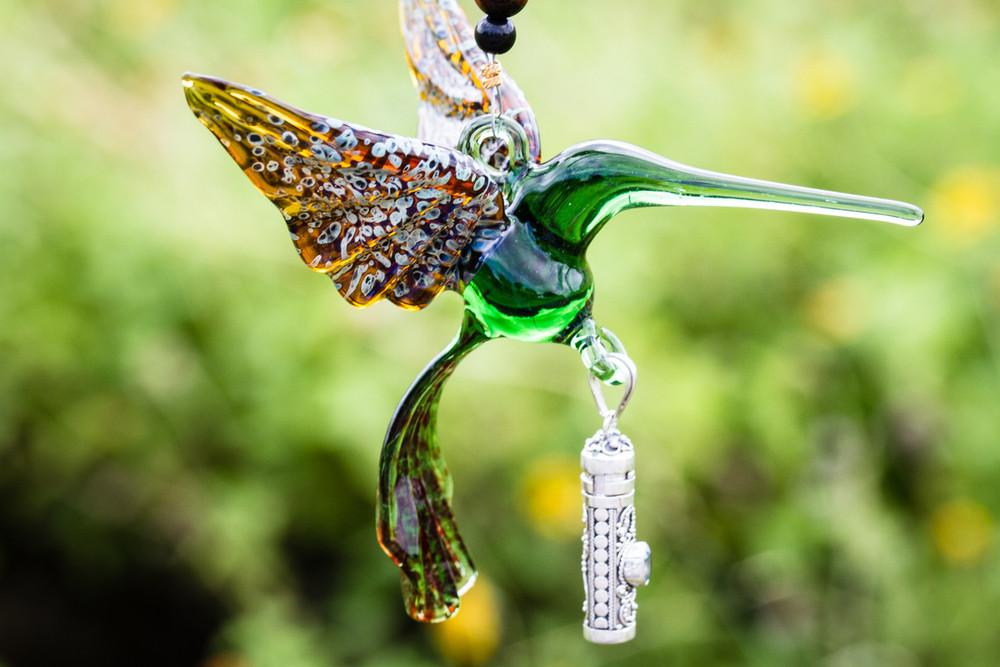 Green glass hummingbird with silver keepsake urn pendant and beaded details shown against a soft green floral background