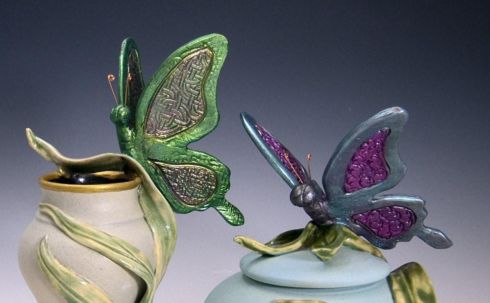 Handmade butterfly ceramic urn featuring a green butterfly perched on a cream vase with a gold rim and leafy accents.
