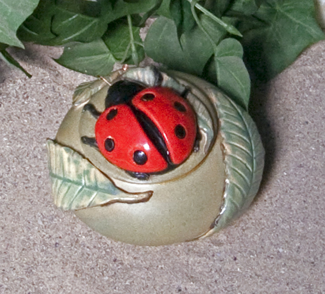 Red ladybug ceramic keepsake urn perched on a white flower with a yellow center viewed from above
