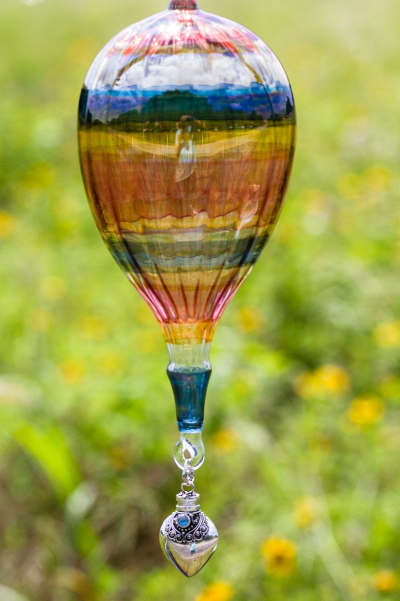Vibrant multicolored glass hot air balloon ornament with a sterling silver keepsake urn pendant hanging from its bottom outdoors.