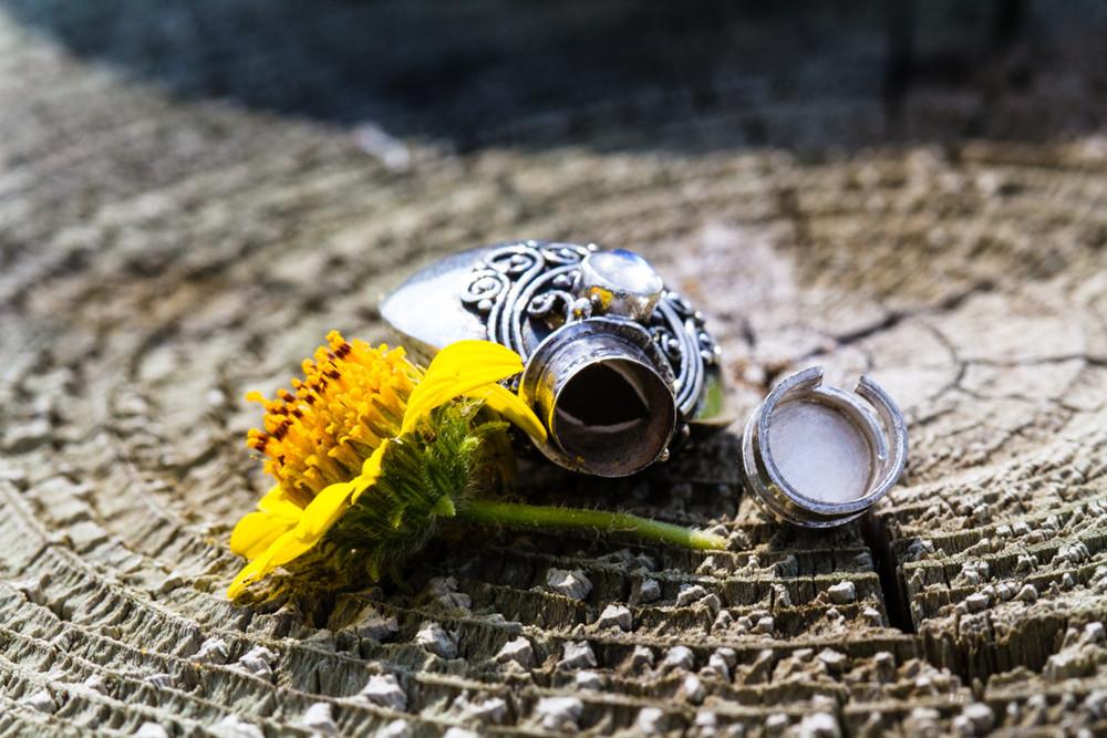 Ornate sterling silver keepsake urn pendant beside a yellow flower on a rustic wood surface