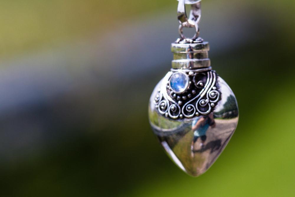 Close-up of a heart shaped silver keepsake urn pendant with intricate filigree and blue stone