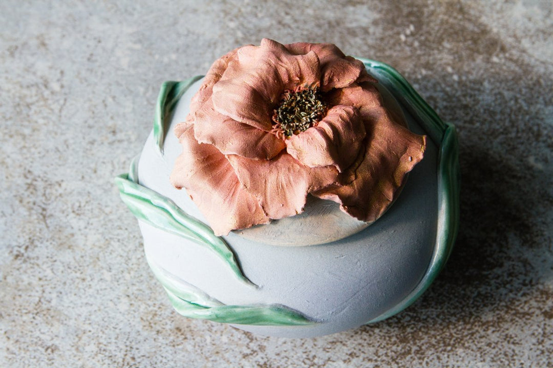Close-up of the pink bloom atop the round ceramic urn with green leaves encircling it.