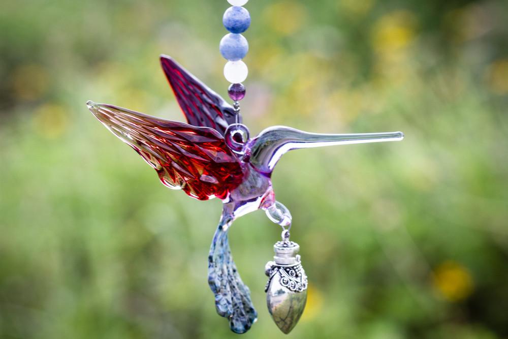 Handmade glass hummingbird with red wings and light purple body, featuring a silver keepsake urn pendant on a beaded string.