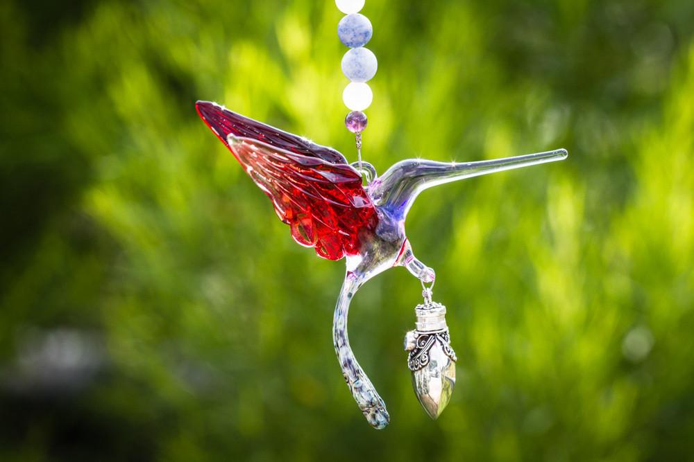 Red and light purple glass hummingbird with a keepsake vial pendant and beaded necklace against a green background.