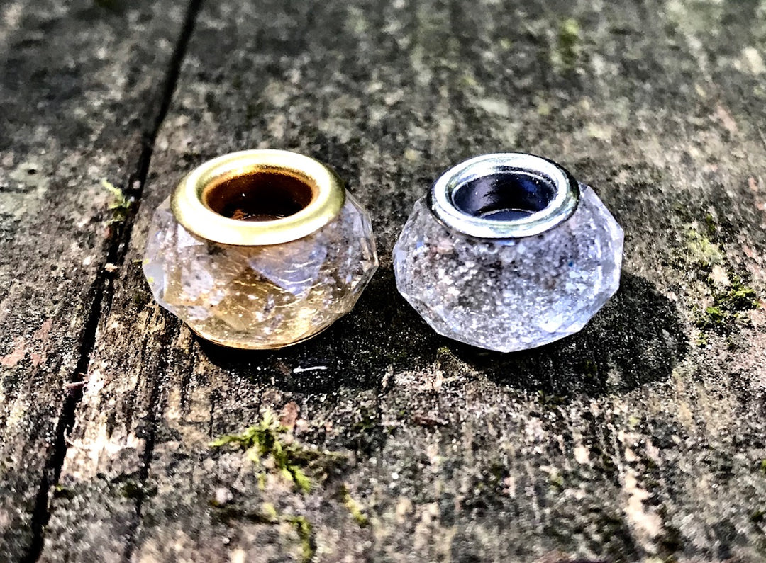 Two faceted crystal beads with gold and silver cores resting on a weathered wood surface