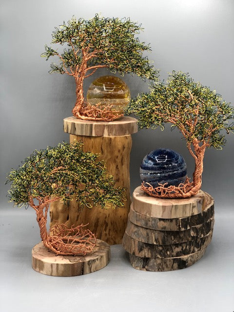 Group of copper wire trees on wooden bases with amber orb on the central pedestal and a blue orb on a lower base.