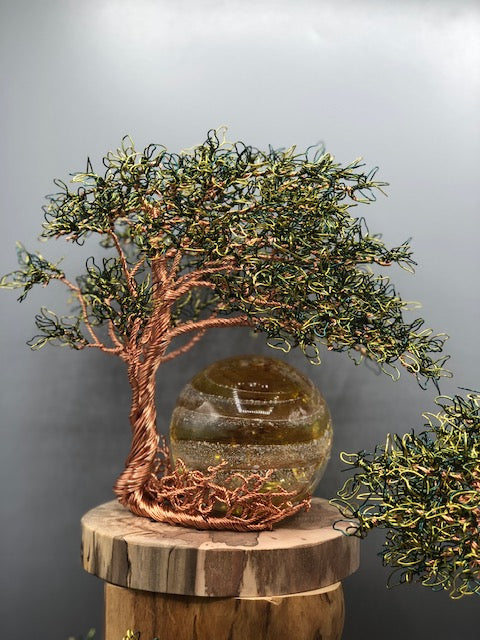 Close up of copper wire tree with amber orb behind the branches on a wooden base.