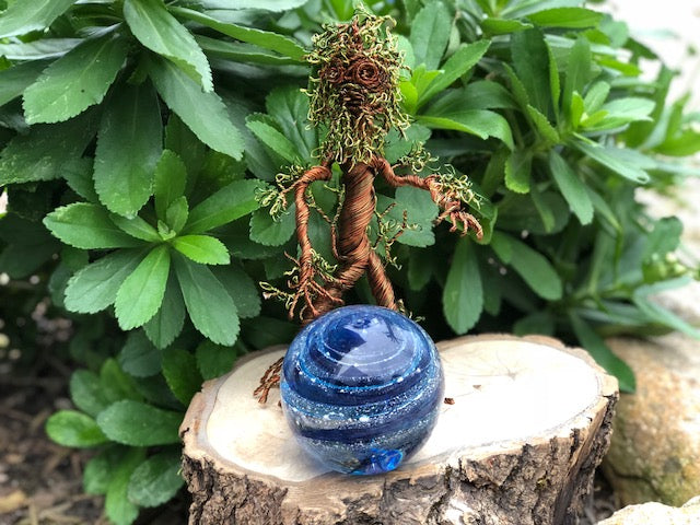 Ent wire sculpture tree with a blue glass orb resting on a wooden log pedestal