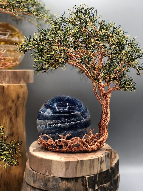 Copper wire tree beside a blue glass orb with white banding on a wooden base.