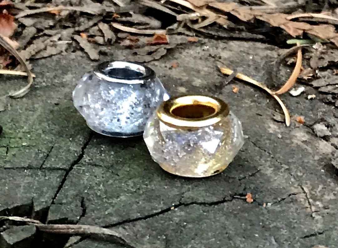 Two crystal-cut cremains beads in silver and gold finishes with visible hollow centers.