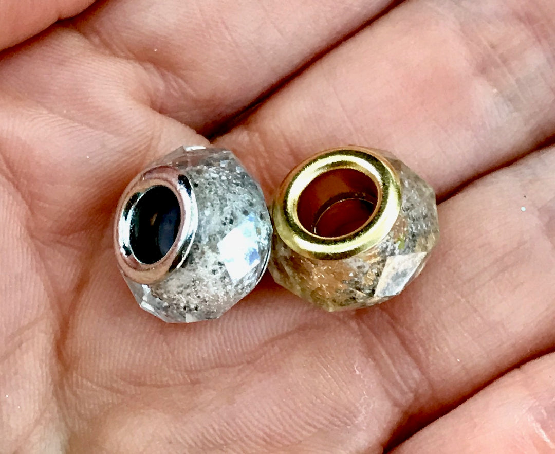Two crystal-cut cremains beads with gold and silver inner rims held in a palm.