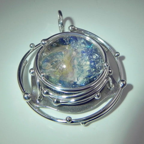 Caged glass galaxy pendant with ashes inside a rotating cabochon surrounded by a silver layered cage.