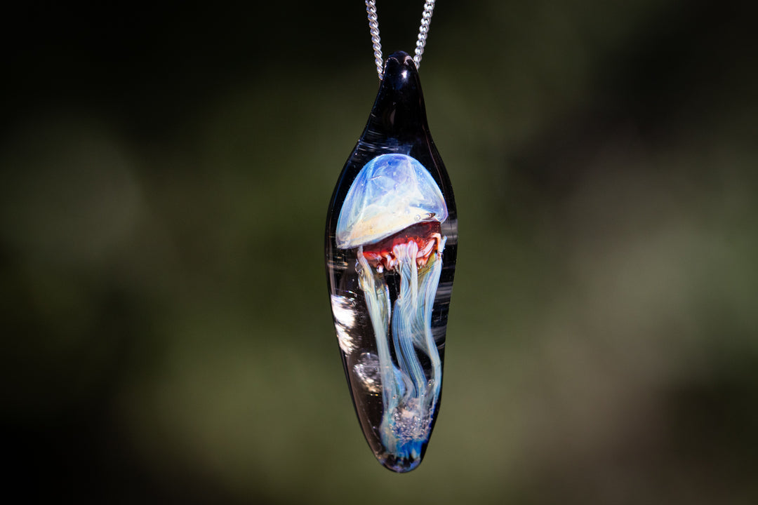 Teardrop glass pendant encasing a blue jellyfish with cremation ash on a black cord