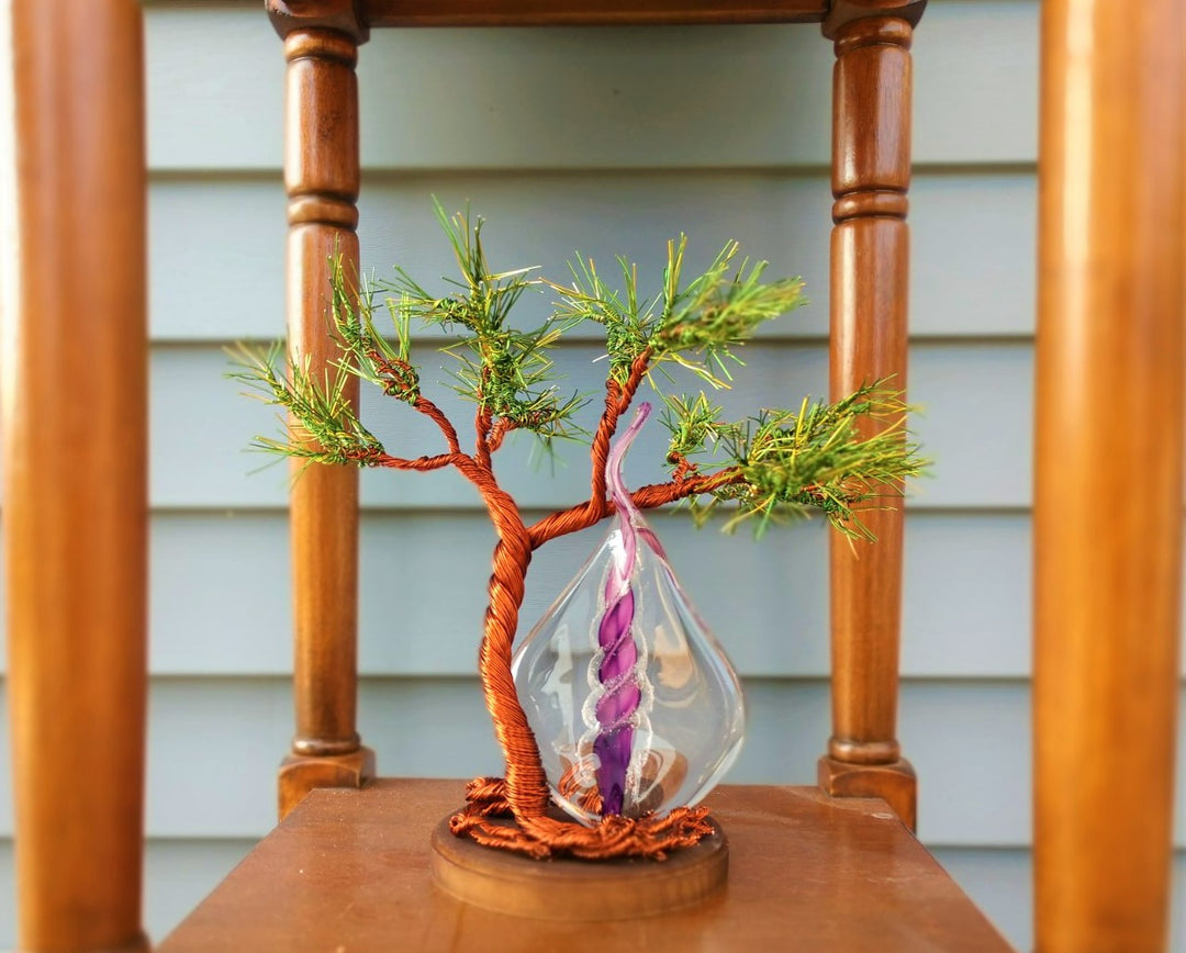 Copper wire tree of life with green pine needles supports a purple glass memorial flame pendant hanging from the branches.