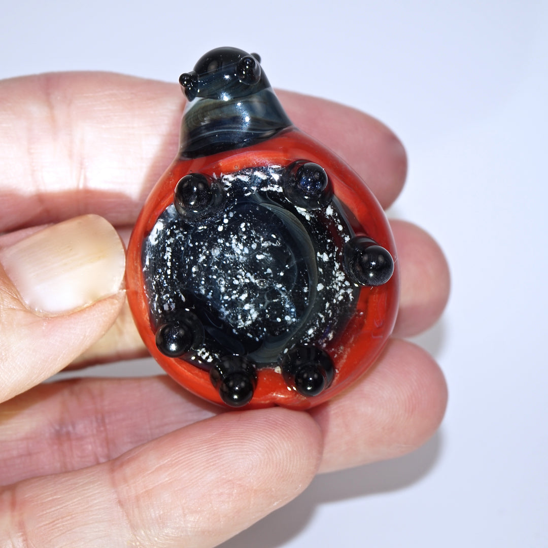 Close-up of red glass ladybug cremains pendant held between fingers