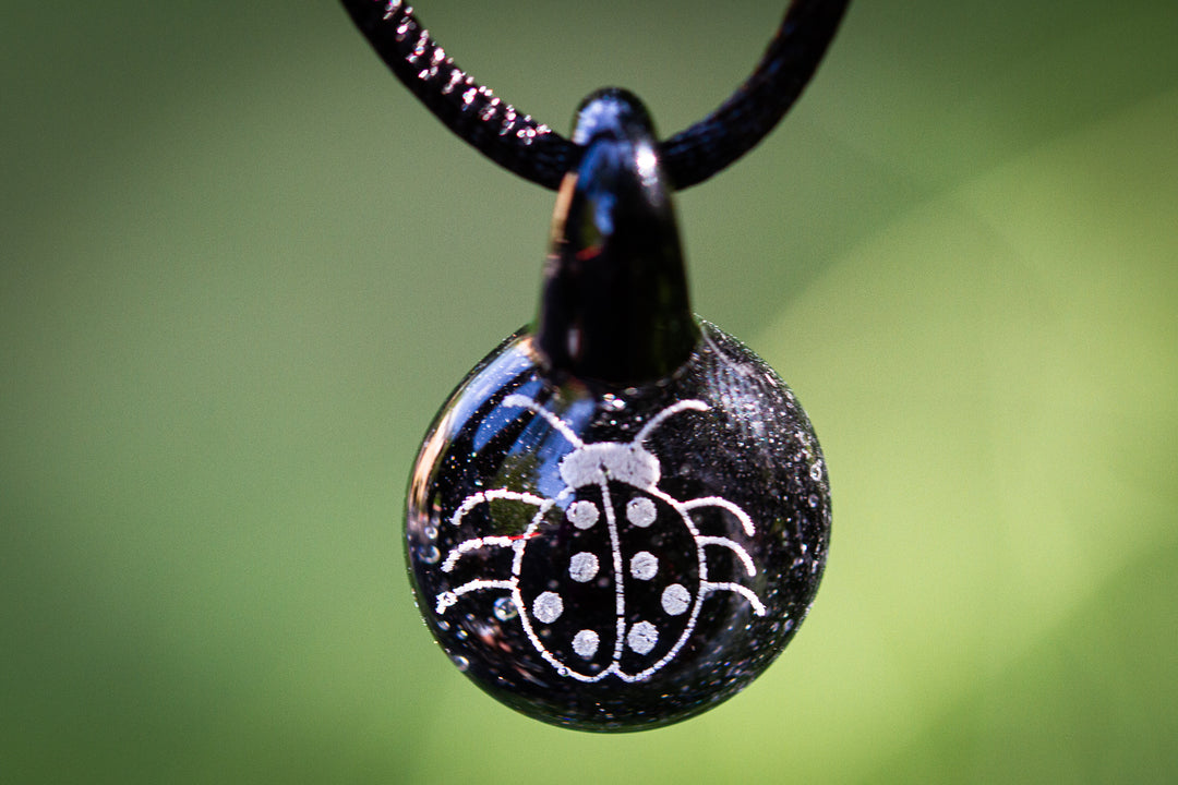 Dark glass pendant with a white holographic ladybug design infused with cremation ash on an adjustable cord.