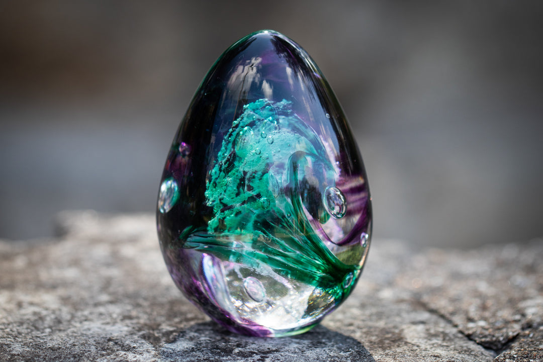 Close-up of a teardrop glass egg with teal green and purple swirls photographed outdoors