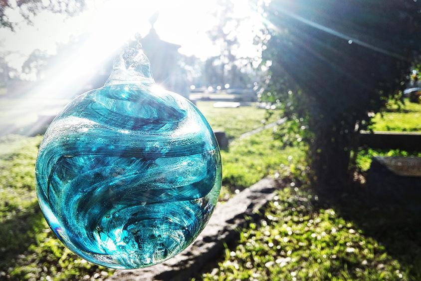 Blue teal rope glass orb with swirling patterns suspended outdoors in bright sunlight