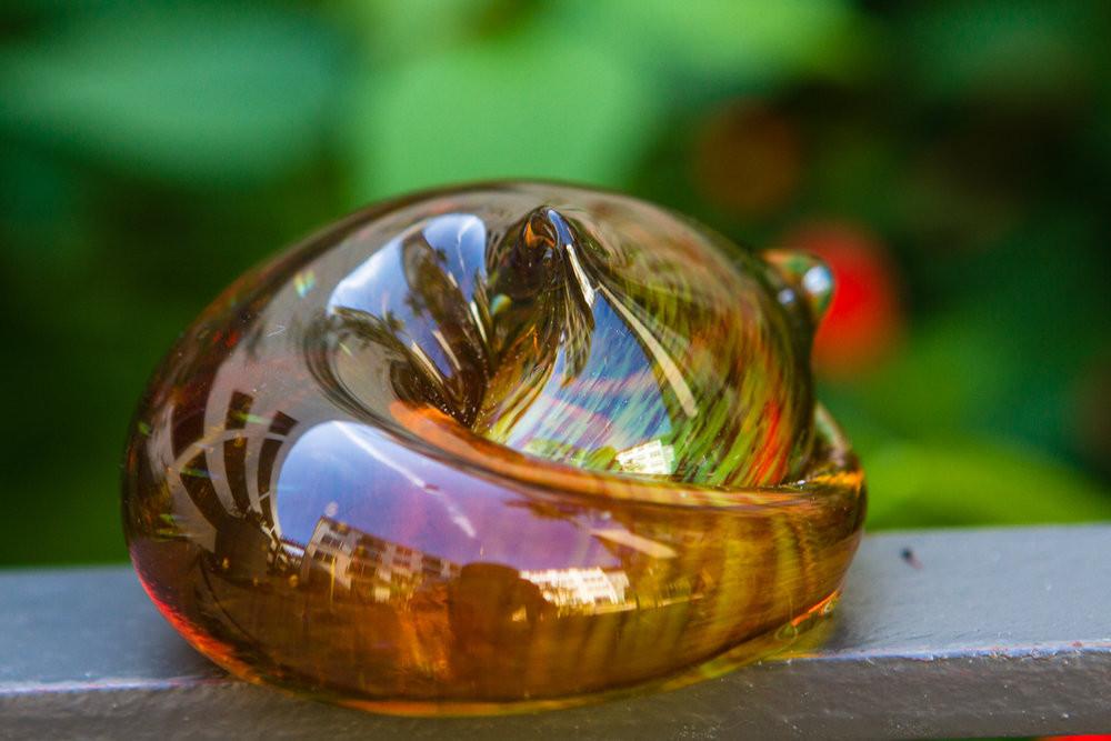 Amber glass cat paperweight with cremains visible beneath clear glass, resting in a hand outdoors.