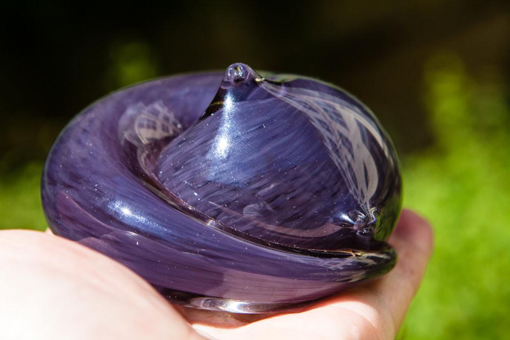 Purple glass cat paperweight with cremains encased under clear glass being held outdoors.