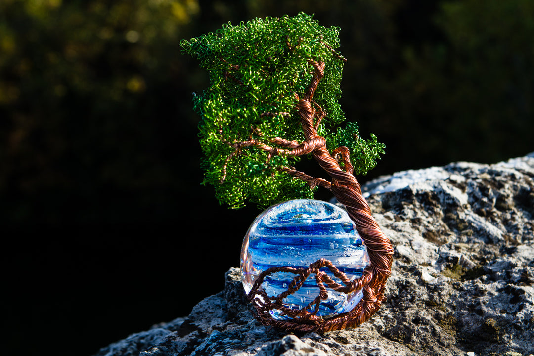Green Ponderosa Tree of Life wire sculpture with blue Bubble Twist Orb on a rocky surface against a dark background