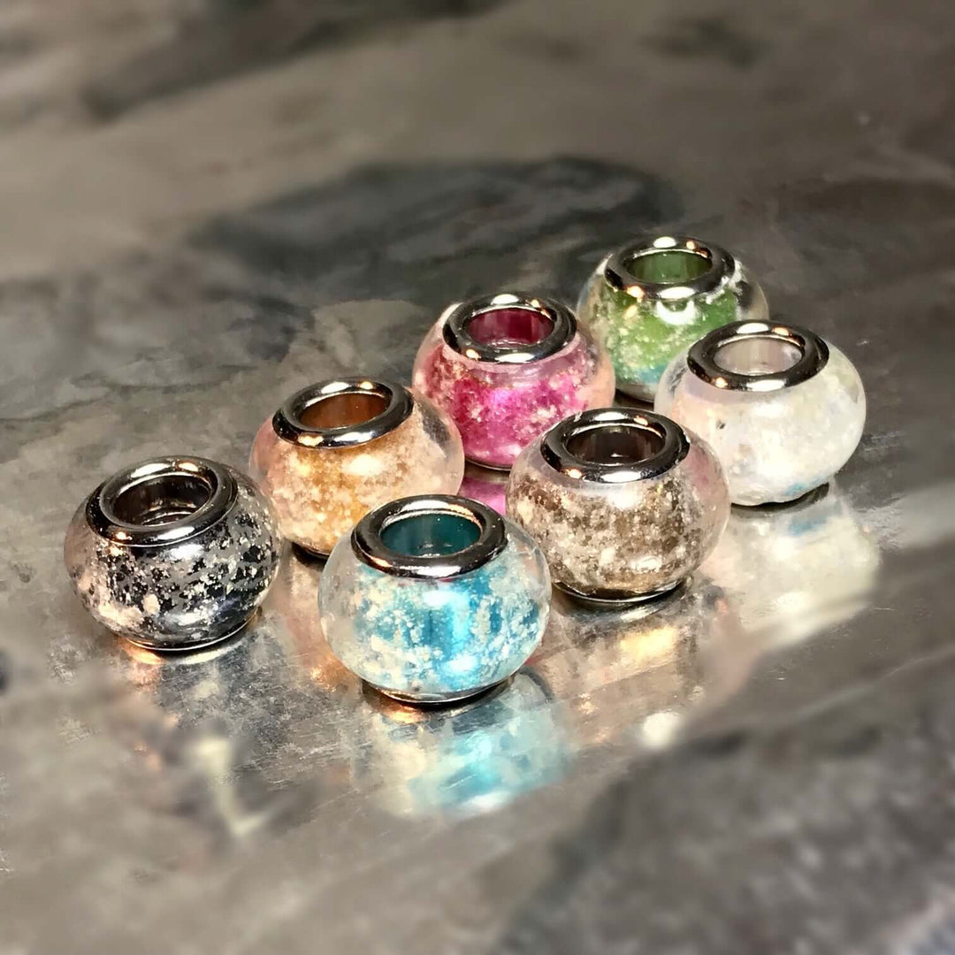 Group of metallic finish cremains beads in blue pink green and other colors on a reflective surface