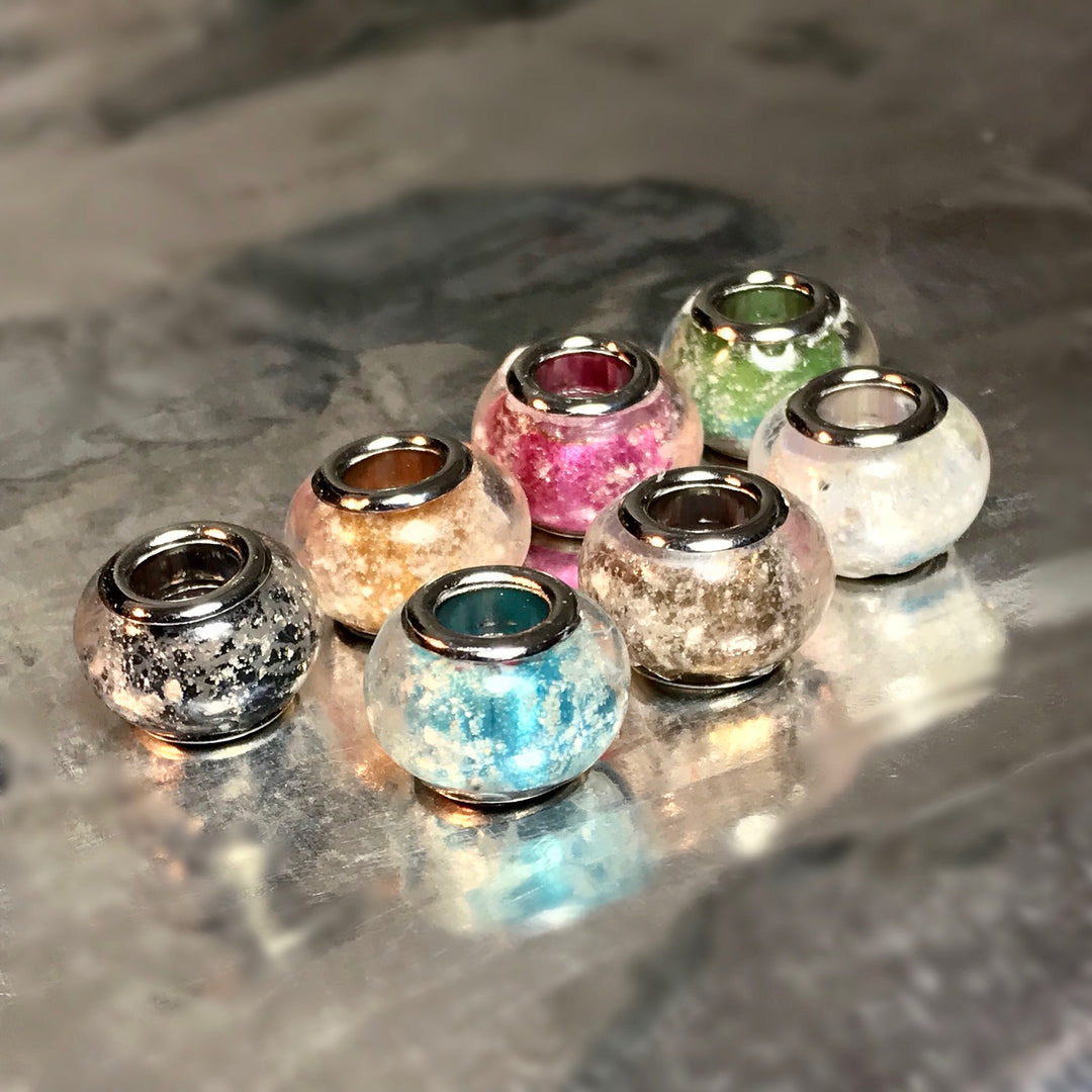 Assorted metallic finish cremation beads with colored interiors arranged on a reflective surface