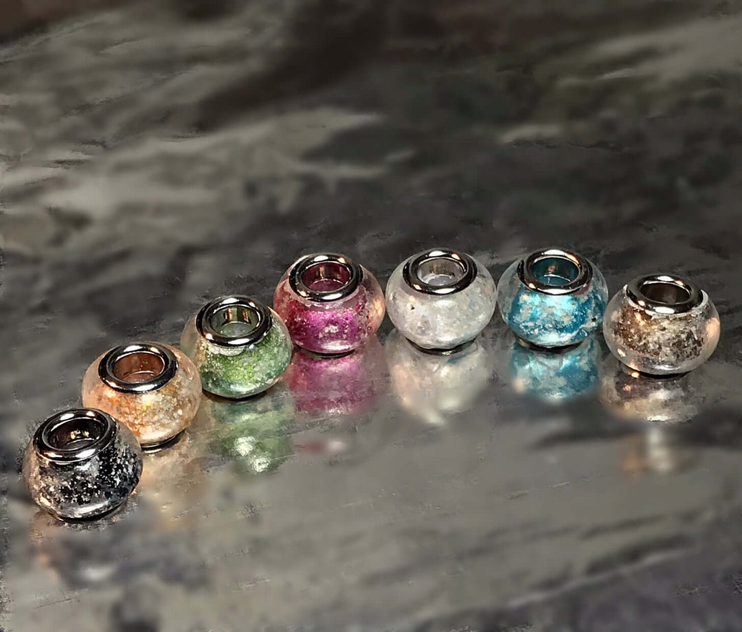 Colorful metallic cremation beads with inner metal cores arranged in a row for Pandora bracelets.