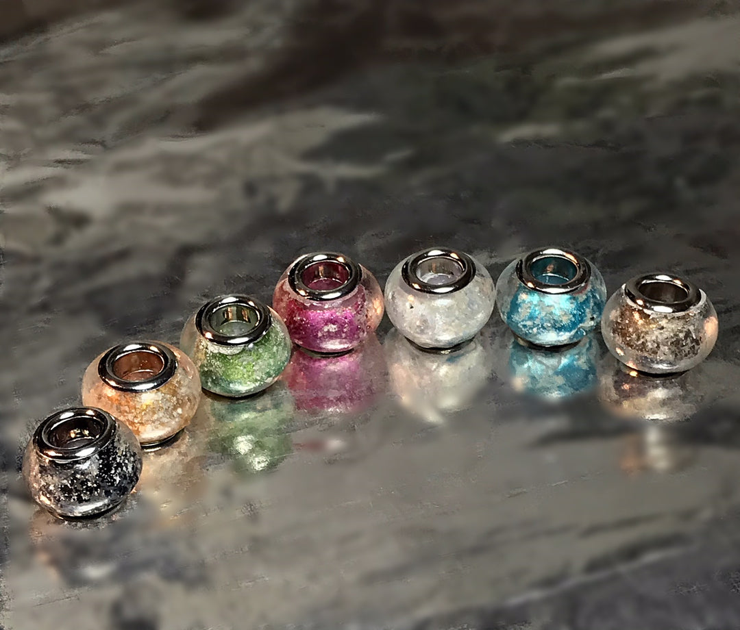 Row of colorful metallic cremation beads with silver rims arranged on a smooth surface