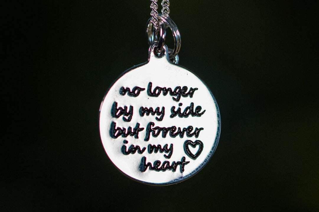 Close-up of a round keepsake pendant with the inscription no longer by my side forever in my heart.