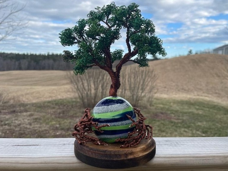 Hand-twisted Oak Tree of Life sculpture on a wooden stand with a striped decorative orb at the base.